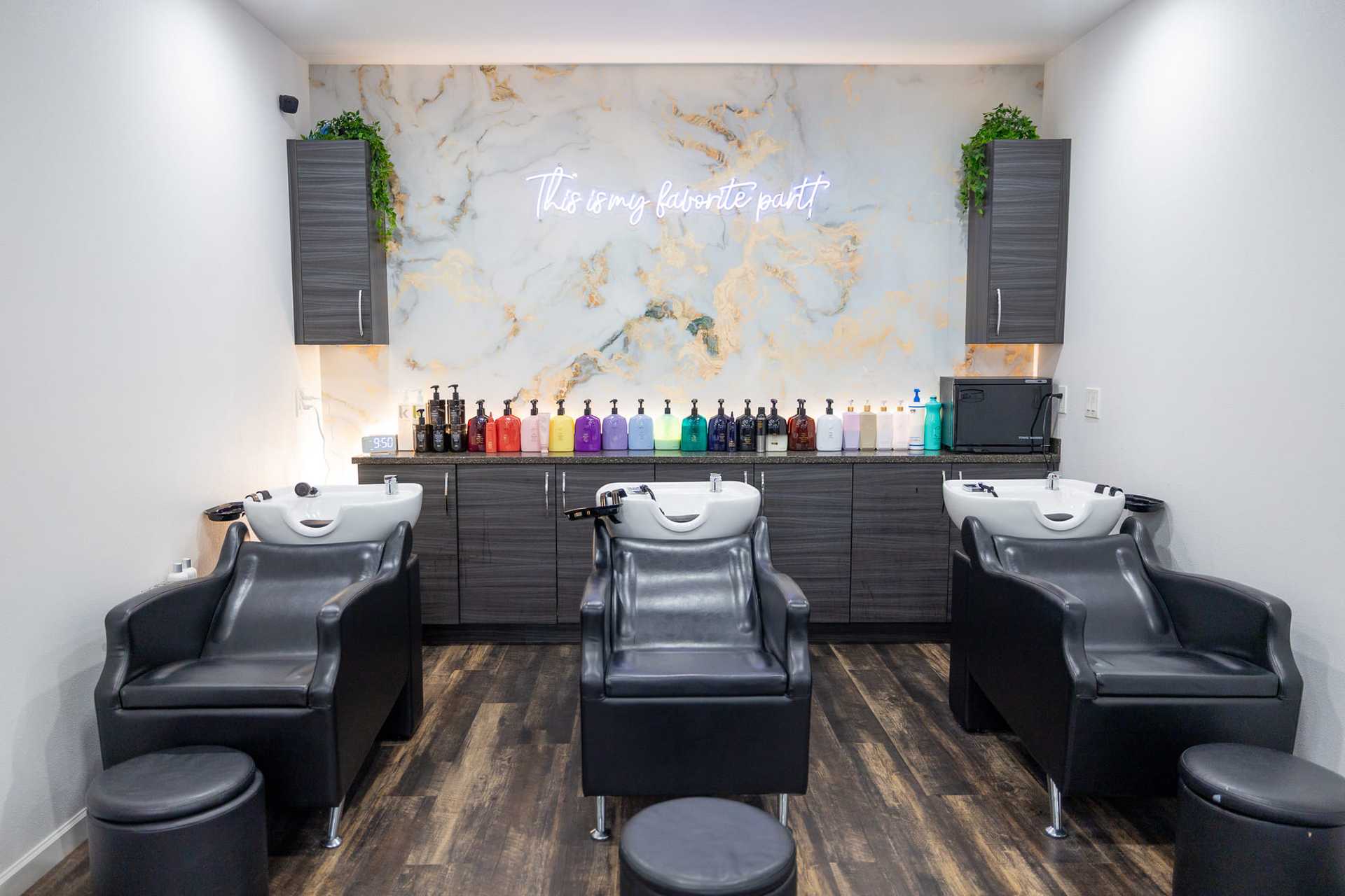 Modern salon shampoo area with black chairs, colorful bottles, and a marble wall sign.